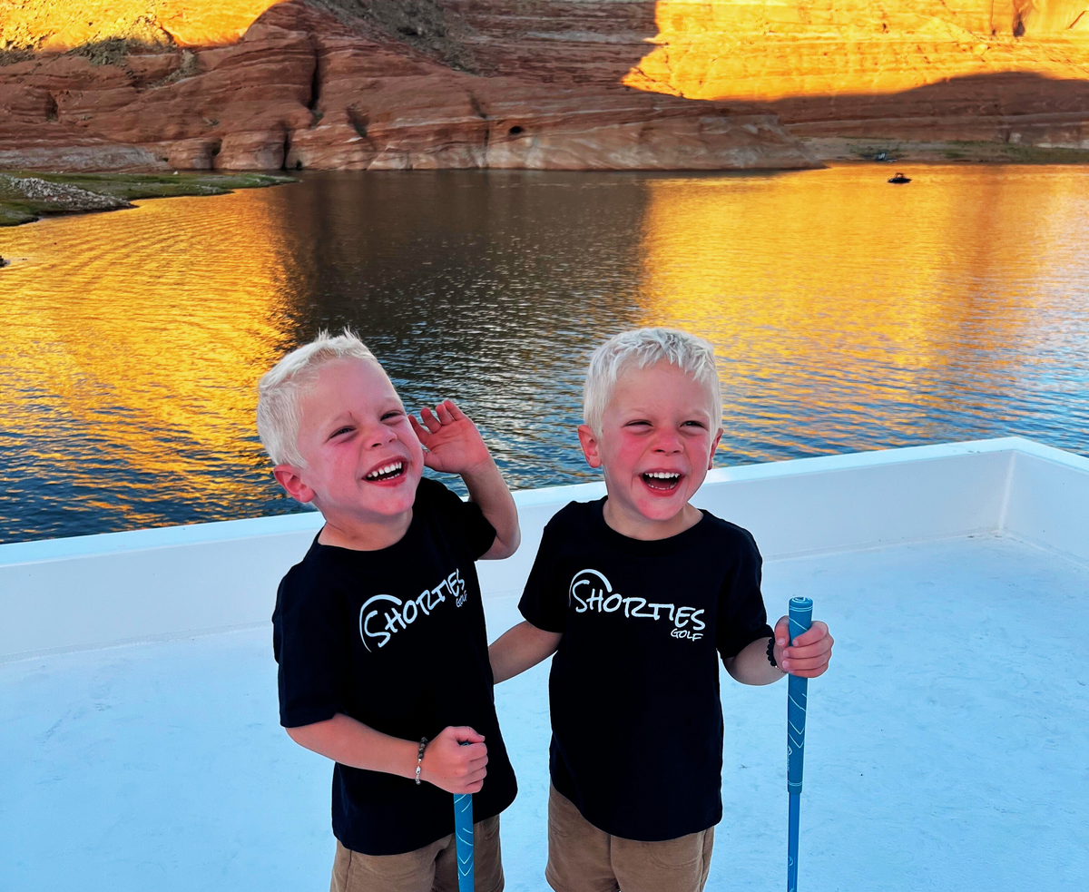 Two young Shorties golfers holding clubs in front of Utah red rock cliffs