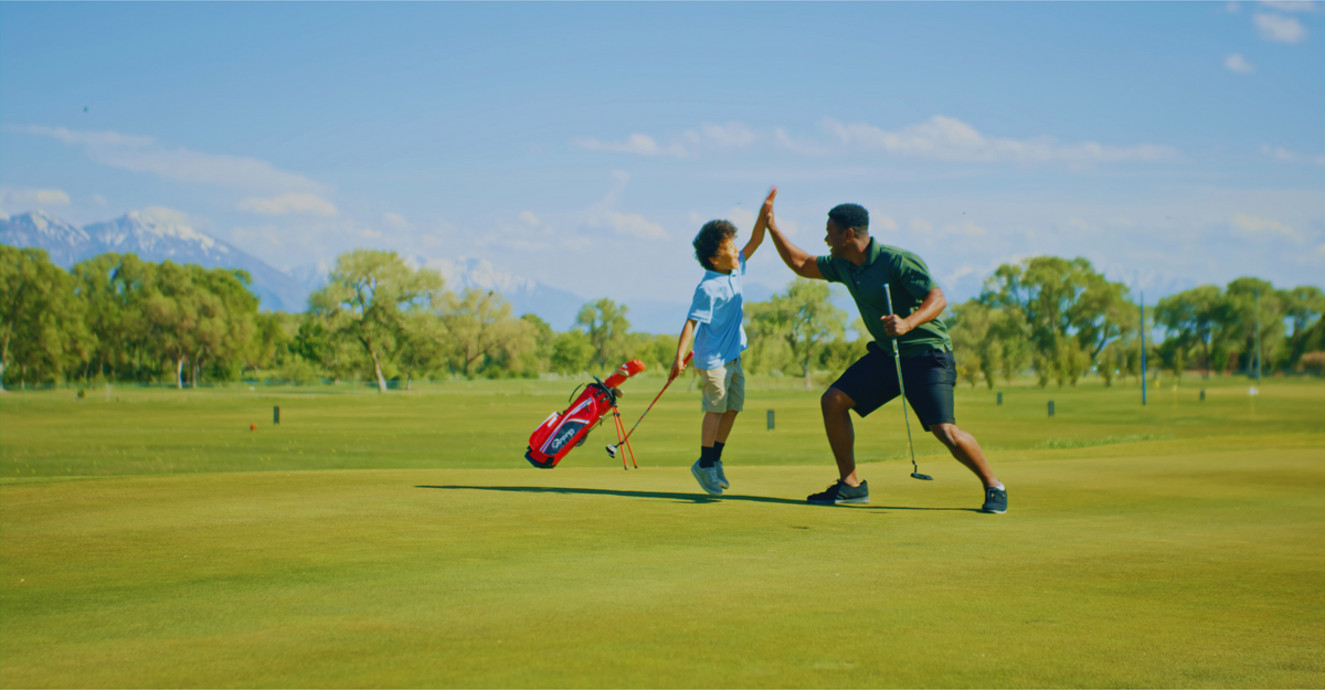 A father and son high-fiving on a golf course with mountains behind them